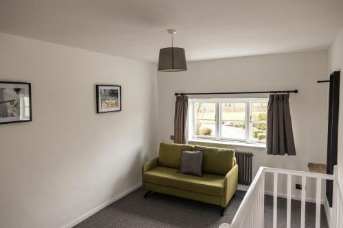 a living room with a green chair and a window at Exclusive Coach House with Lakeside Hot Tub on Country Estate in Toddington