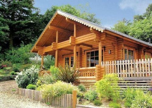 una cabaña de madera con una valla delante en Solid Log Cabin With Private Hot Tub - Oak, en Aymestrey
