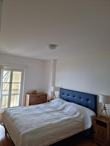 a bedroom with a bed with a blue headboard and a window at L'Appartement et Le Studio in Chexbres