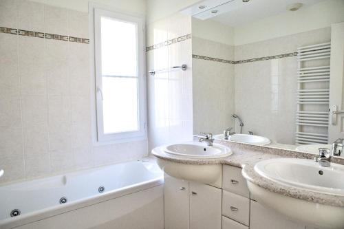 ein weißes Badezimmer mit zwei Waschbecken, einer Badewanne und einem Fenster in der Unterkunft villa familiale dans cadre exceptionnel, piscine chauffée-AG19 in Lacanau