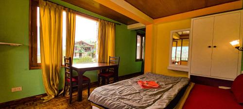 a bedroom with a bed and a desk and a window at La Vaca India Manali in Manāli