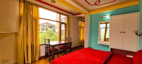 a bedroom with a bed and a table and a window at La Vaca India Manali in Manāli