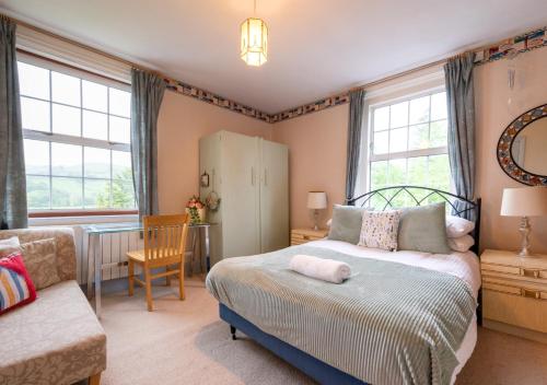 a bedroom with a bed and a chair and windows at Aberhiriaeth Hall in Cemmaes