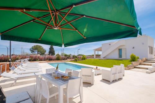 a pool with white chairs and a green umbrella at Villa Palamita Luxury - Specchia in Specchia