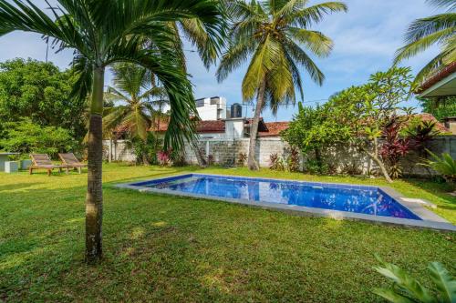 a swimming pool in the yard of a house with a palm tree at Ocean Gate Negombo in Negombo
