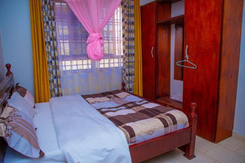 1 dormitorio con 1 cama y una ventana con cortinas rosas en J & A VILLAS, en Mbale
