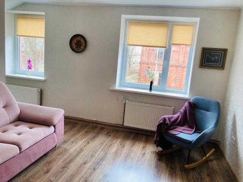a living room with a couch and a chair and two windows at Nākotnes street apartaments in Liepāja