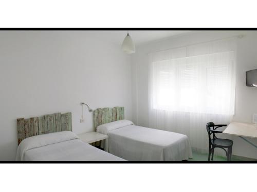 two beds in a room with a table and a chair at Hotel Langosteira in Finisterre