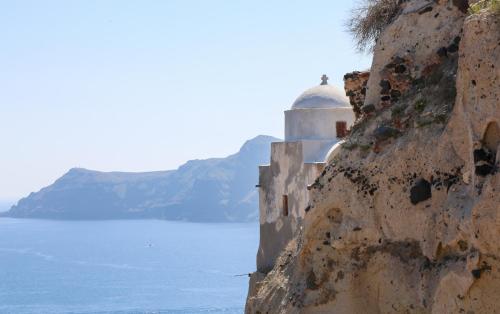 a building on the side of a cliff next to the water at Oia VineyART Homes in Oia