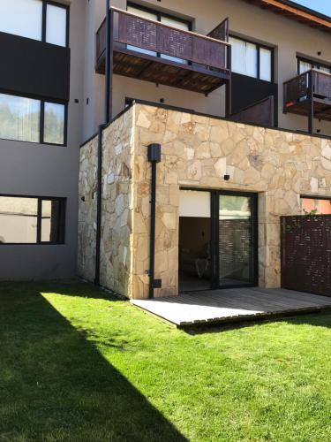 una casa con una fachada de piedra y un patio de césped en AIKEN JARDIN con cochera en San Martín de los Andes