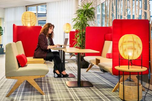 a woman sitting at a table with a laptop at Novotel Senart Golf De Greenparc in Saint-Pierre-du-Perray