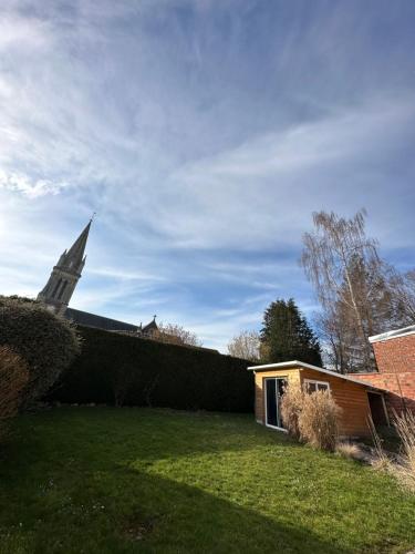 a church with a steeple in the background with a yard at Le cocoon in Forges-les-Eaux