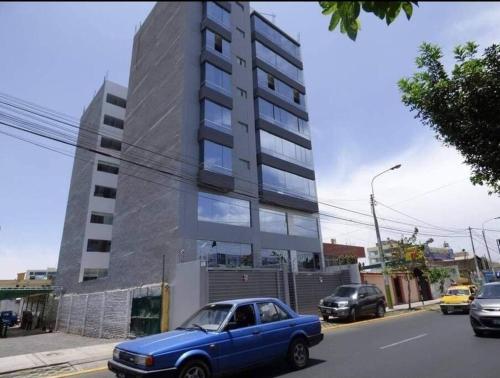 a blue car parked in front of a tall building at ApartHotel moderno y céntrico por la Av. Dolores in La Pampilla