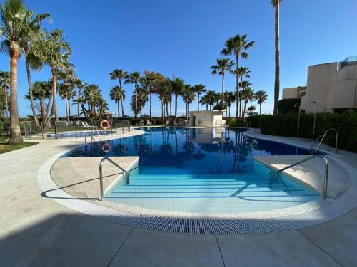 a swimming pool with palm trees in a resort at Apartamento lujo en primera línea de playa en Bahía de la Plata, Estepona in Estepona