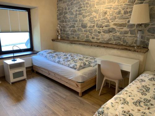 een slaapkamer met 2 bedden, een bureau en een stenen muur bij Les Myosotis in Assesse