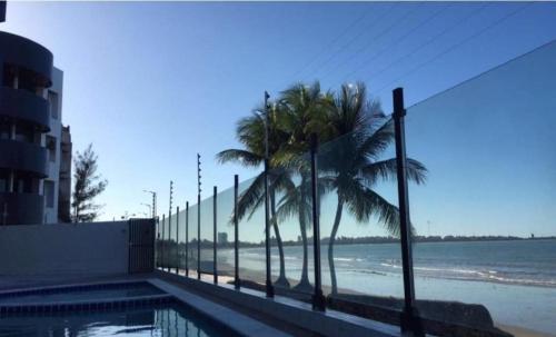 uma vista para uma praia com uma cerca e palmeiras em Apartamento Pé Na Areia - Praia do Bessa - PB em João Pessoa