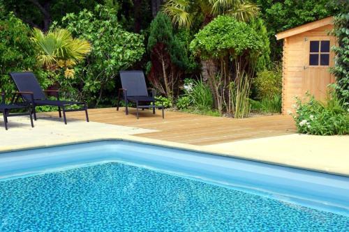 una piscina con 2 sillas y una terraza de madera en Maison de charme avec piscine, en Clohars-Carnoët
