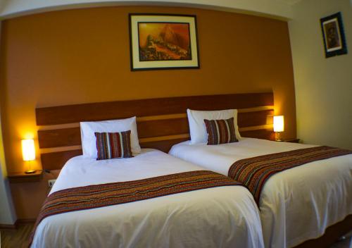 two beds in a hotel room with two lamps at Hotel Chinchero Boutique & Tours in Chinchero