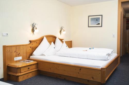 a bedroom with a wooden bed with white sheets and pillows at Hotel Die Arlbergerin - Design & Tiroler Gemütlichkeit in Sankt Anton am Arlberg