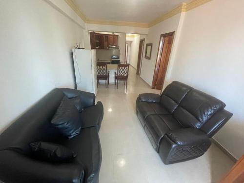 a living room with a black leather couch and a kitchen at Aparta Hotel Caribe Paraiso in Juan Dolio