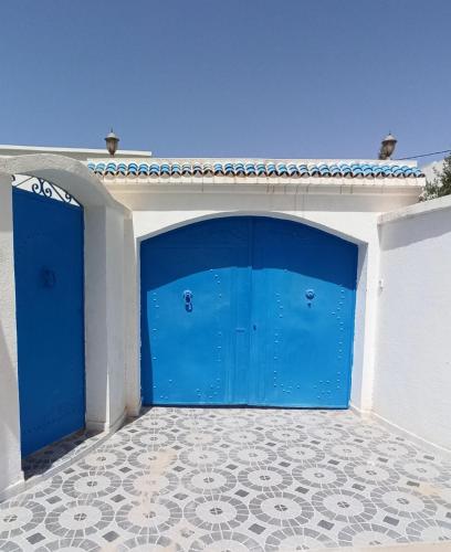 2 puertas azules de garaje en un edificio con suelo de baldosa en Waneshouse دار الونس (Djerba), 