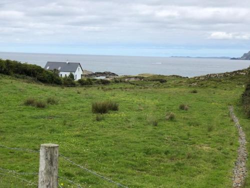 a fence in a field with a house and the ocean at An teach Illanmore in Portsalon