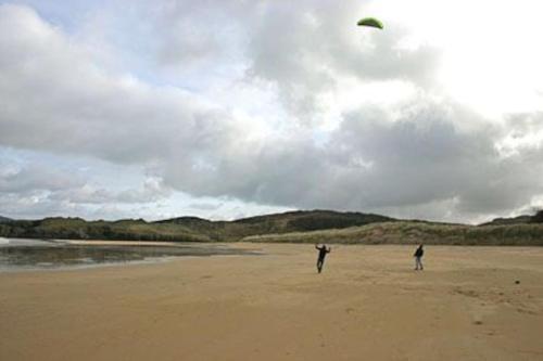 two people are flying a kite on the beach at An teach Illanmore in Portsalon