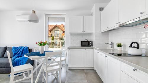 a kitchen with white cabinets and a table with chairs at BURSZTYNOVA Apartamenty Piamola in Kąty Rybackie