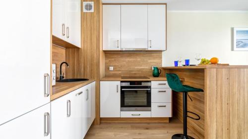 a kitchen with white cabinets and a green chair at BURSZTYNOVA Apartamenty Piamola in Kąty Rybackie