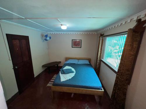 a small bedroom with a blue bed and a window at Pura Vida Hostel in Montezuma