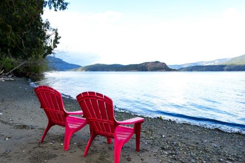 two red chairs sitting on the beach near the water at Sea and Cedar Retreat-a home in a tranquil setting in Cowichan Bay