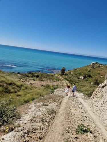 two people walking down a dirt road near the ocean at Tendu' Punta Bianca Glamping Camp in Palma di Montechiaro