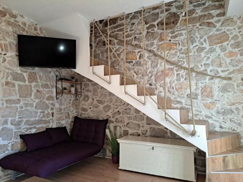 a living room with a couch and a tv on a stone wall at Kuća Get in Betina