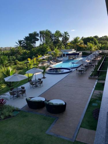 a resort with a swimming pool and tables and umbrellas at Apartamento em Guarajuba - Condomínio Paraíso dos Coqueiro in Guarajuba