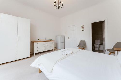 a white bedroom with a bed and a dresser and a refrigerator at Spacious Ensuite Room Near Top Tourist Attractions in London