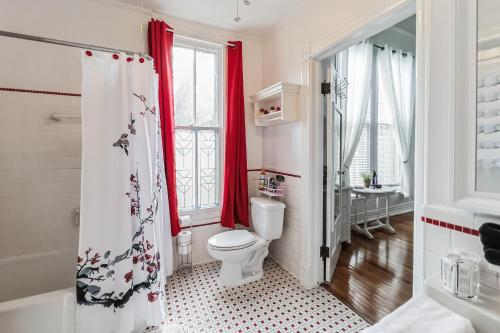 a bathroom with a toilet and a window with red curtains at Baker Street Bed and Breakfast in Eufaula