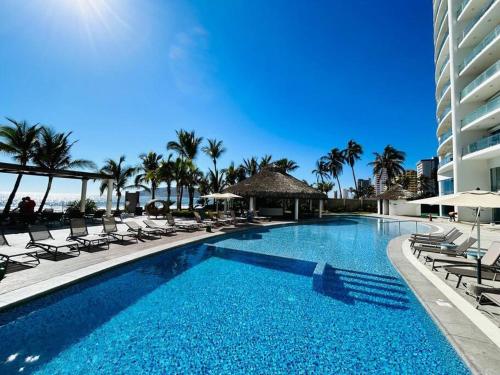 a swimming pool with lounge chairs and a building at Lujoso departamento frente al mar/camino al mar in Mazatlán