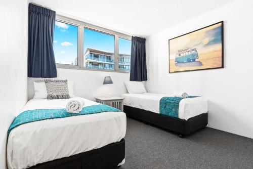 two beds in a room with two windows at Northwind Beachfront Apartments in Mooloolaba