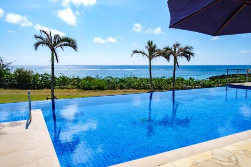 a swimming pool with palm trees and the ocean at Allamanda Imgya Coral Village in Miyako-jima