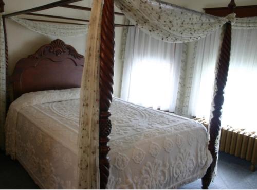 a bedroom with a canopy bed with white sheets and windows at Tarry Here Mansion Bed & Breakfast in Salamanca