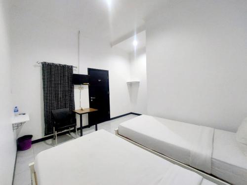 a white room with two beds and a chair at COZY STAY KUPANG in Kupang