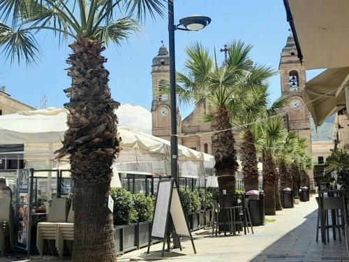 a palm tree in front of a building with a clock tower at Terra Sinus Holiday House in Terrasini