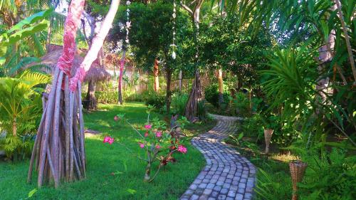 einen Kopfsteinpflasterweg in einem Garten mit Bäumen und Blumen in der Unterkunft UTOPIA in Gili Air