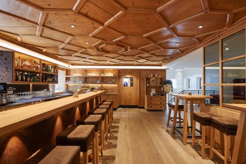 a bar with wooden ceilings and wooden stools at Après Post Hotel in Stuben am Arlberg