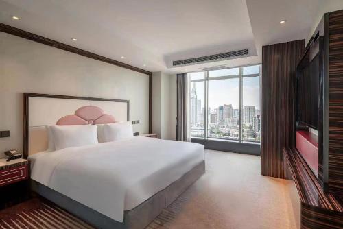 um quarto com uma grande cama branca e uma grande janela em Suning Universal Hotel ALL-SUITES em Nanquim