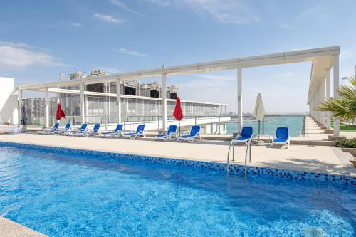 une piscine avec des chaises bleues et un bâtiment dans l'établissement Luxury 1BR Beachfront Apartment Marjan Island, à Ras al Khaimah