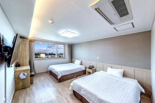 um quarto de hotel com duas camas e uma televisão em SH Jungmoon City Stay em Seogwipo