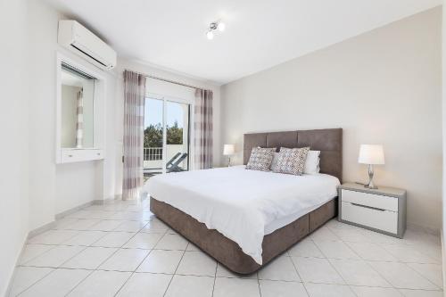 a white bedroom with a large bed and a window at Apartament Portes Balaia in Albufeira