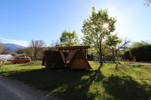 a wooden structure sitting in the grass next to a road at Habitat Créateur - Hébergements insolites au camping municipal "Les Ecureuils" in Recoubeau