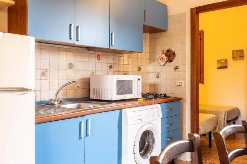 a kitchen with blue cabinets and a washer and dryer at Il Glicine Cala Lupo in Stintino